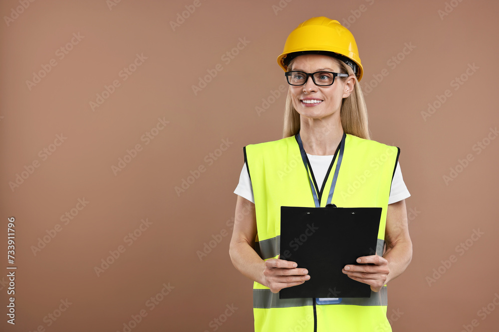 Engineer in hard hat holding clipboard on brown background, space for text Engineer in hard hat holding clipboard on brown background, space for text
