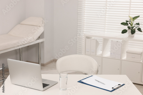 Doctor's workplace. Laptop, clipboard and glass of water on white table in hospital