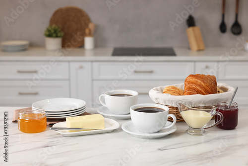 Breakfast served in kitchen. Fresh croissants, coffee, butter, jam, honey and sweetened condensed milk on white table