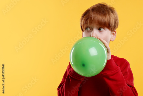 Boy inflating green balloon on orange background, space for text