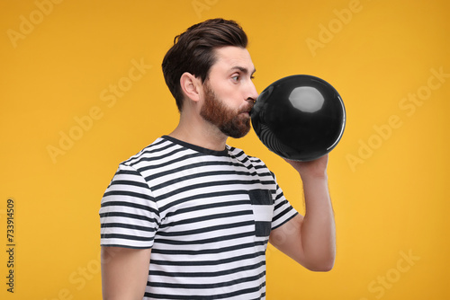 Man inflating black balloon on yellow background