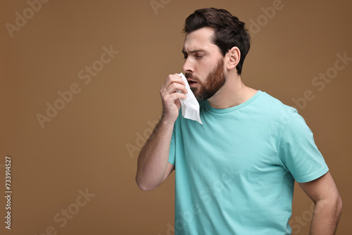 Sick man with tissue coughing on brown background  space for text