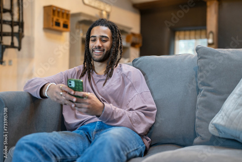 Man with dreads relaxing on sofa and using phone