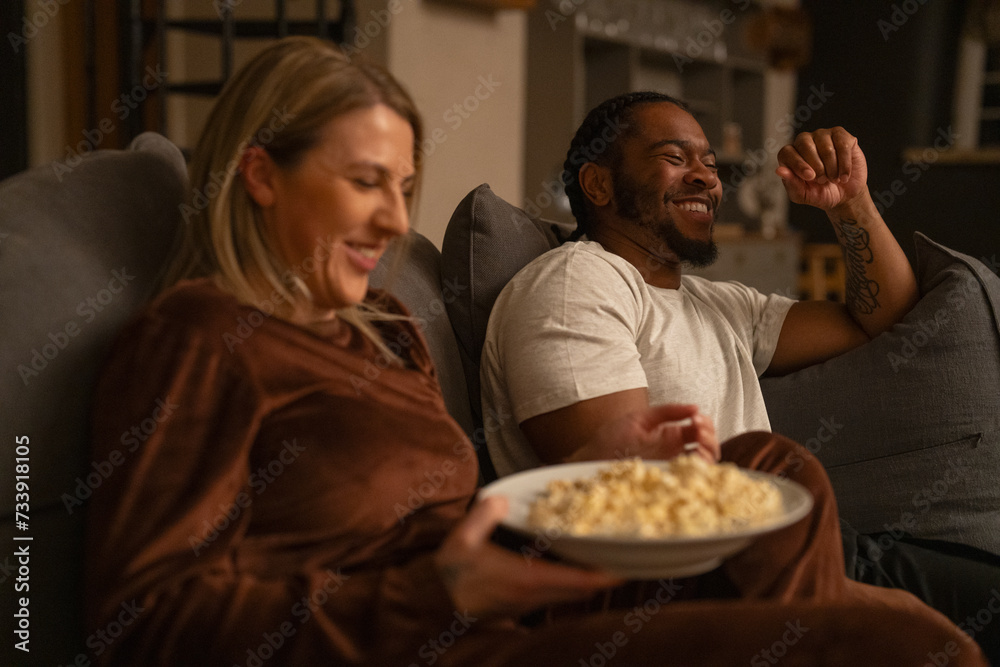 Smiling friends relaxing on sofa at home, sharing popcorn Smiling friends relaxing on sofa at home, sharing popcorn