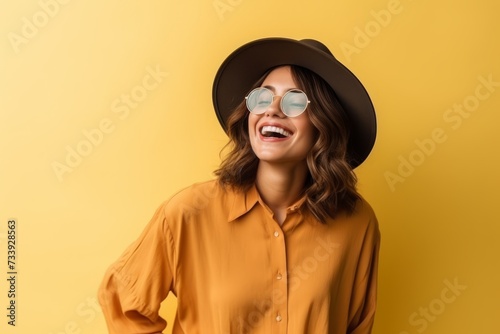 stylish young woman in hat and sunglasses laughing at camera isolated on yellow © Iigo
