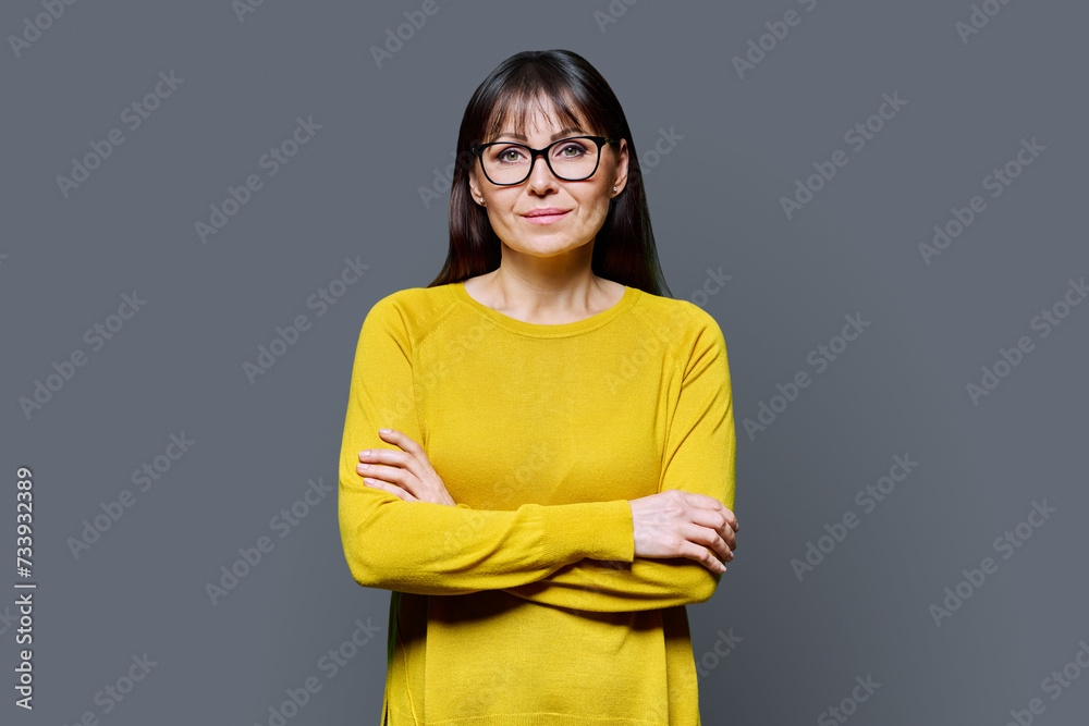 Portrait of smiling mature confident woman with crossed arms on dark gray studio background Portrait of smiling mature confident woman with crossed arms on dark gray studio background