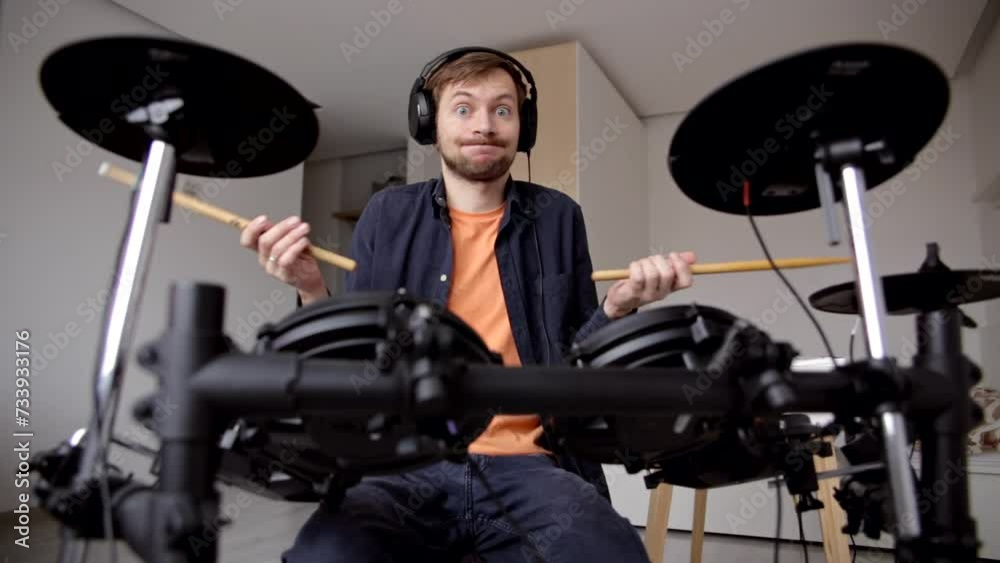 Confused man drummer beginner with headphones trying to play electric drum at home