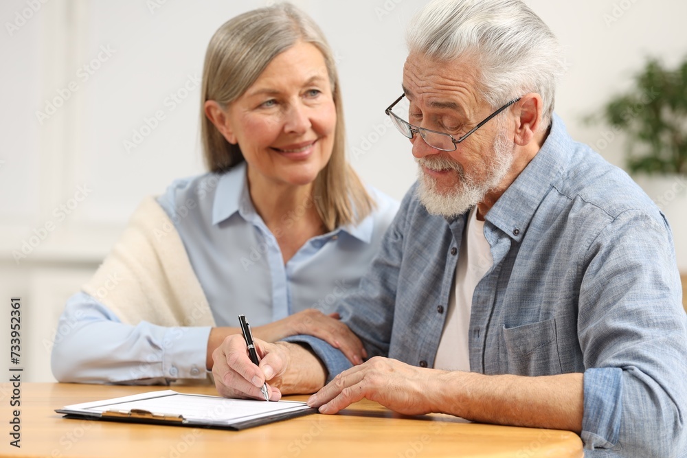 Happy senior couple signing Last Will and Testament indoors Happy senior couple signing Last Will and Testament indoors