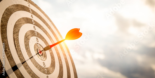 Close up shot red darts arrows in the target  of dartboard center on dark blue sky background. Business target or goal success and winner concept. photo