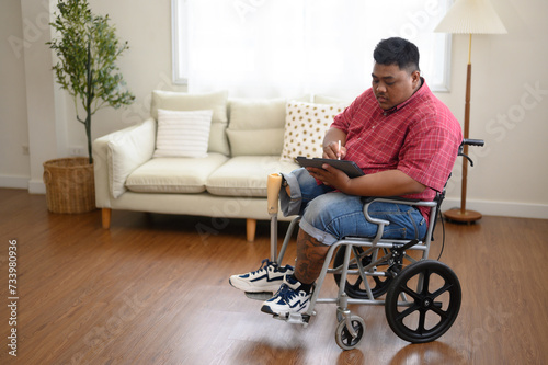 A big fat man sits on a wheelchair and uses a tablet.