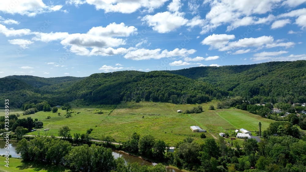 Peaceful countryside landscape in Olean, NY with river, hills, green pastures under blue sky and clouds