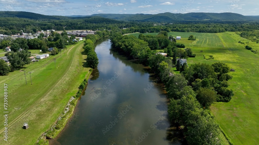 Peaceful countryside landscape in Olean, NY with river, hills, green pastures under blue sky and clouds