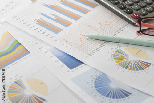 graphs and charts. business reports and pile of documents with a coffee cup, glasses, pen, calculator place on desk.