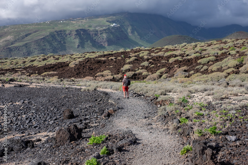Rear view of an elderly man walking in the nature of Malpais de Guimar at Tenerife island with backpack on his shoulder