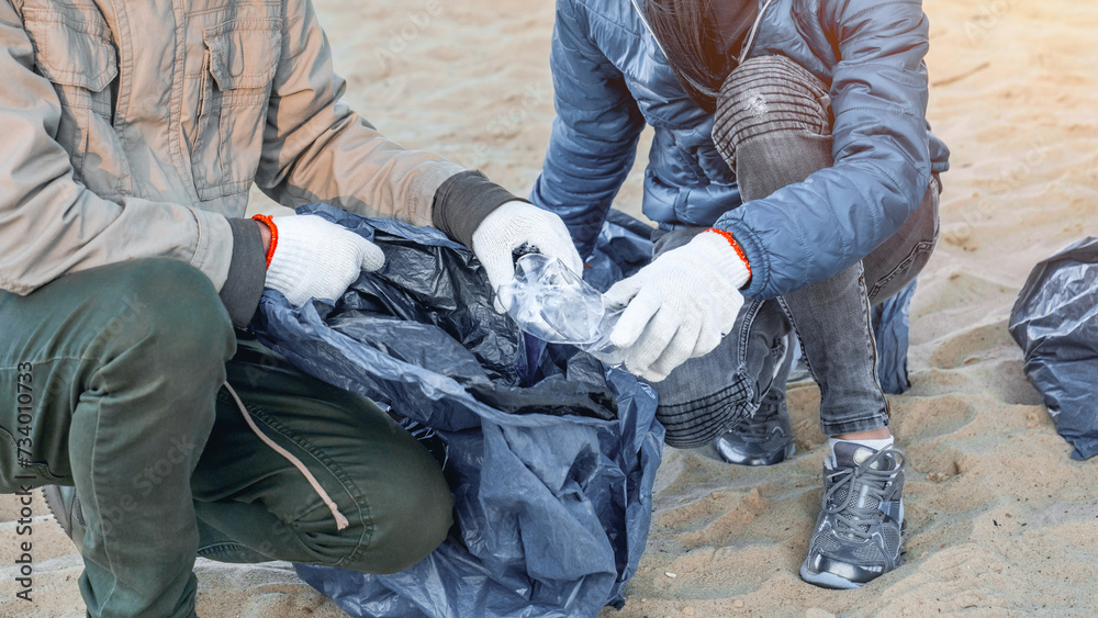 Unrecognizable young man picking up plastic trash with group of volunteers on the beach. Zero-waste concept. Recycling. Earth Day. Environment conservation Unrecognizable young man picking up plastic trash with group of volunteers on the beach. Zero-waste concept. Recycling. Earth Day. Environment conservation