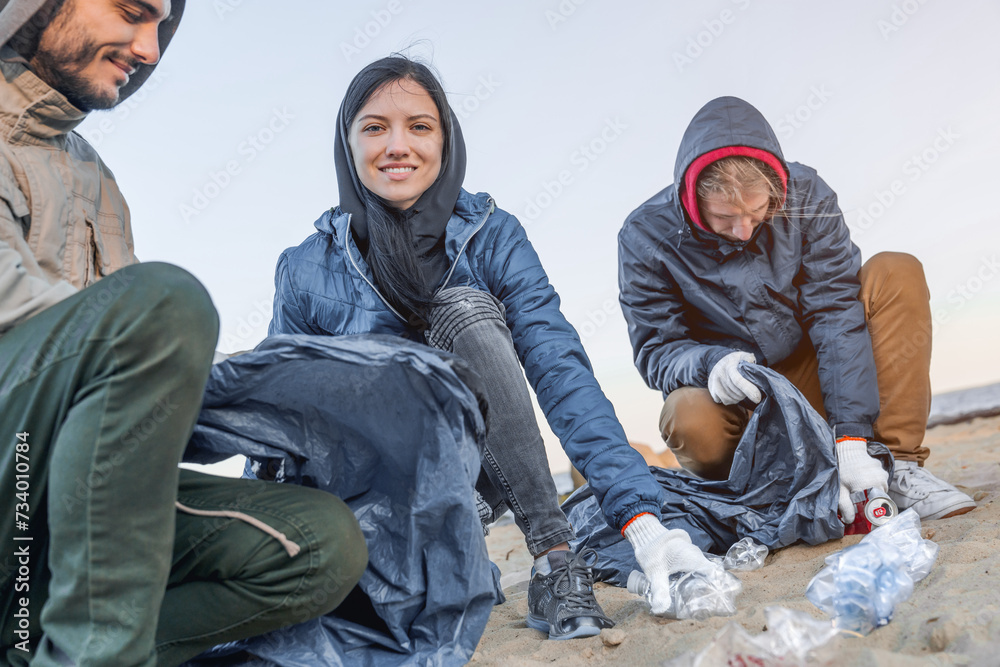 Environment concept. Young people picking up trash on the beach, pretty young girl smiling and looking at camera. Eco-activists environmentalists preventing plastic pollution