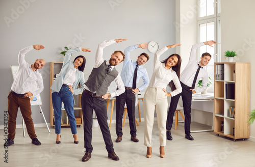 Fototapeta Naklejka Na Ścianę i Meble -  Happy young business people doing stretching sport exercises standing together in modern office. Group of smiling company employees exercising fitness for health during a break from a work.