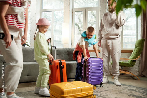 Photo of family with colorful luggage, preparing for travel in living room at home. Parents and children playful and ready to adventures. Concept of tourism, holiday, vacation, relaxation. Ad