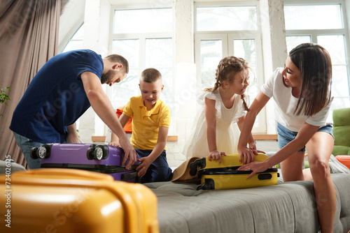 Parents help their children to packing clothes in living room at home before leaving for children's health camp. Joyful mood before trip. Concept of tourism, holiday, vacation, relaxation. Ad photo