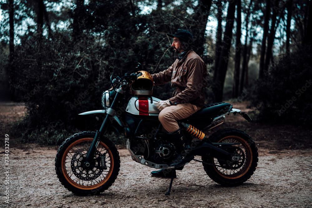 Hombre moreno con moto dentro de un bosque posando y montando por terreno silvestre