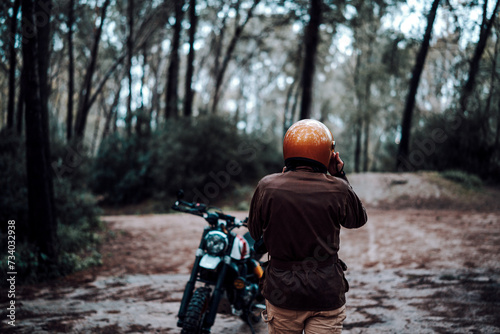 Hombre moreno con moto dentro de un bosque posando y montando por terreno silvestre