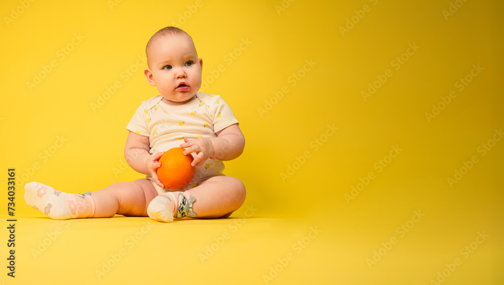 Beautiful baby girl holds orange sitting in studio on yellow background. Beautiful baby girl holds orange sitting in studio on yellow background.