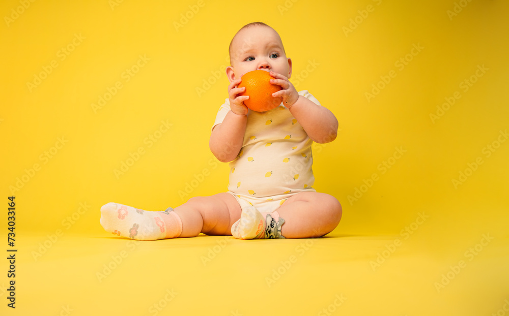 Beautiful baby girl holds orange sitting in studio on yellow background. Beautiful baby girl holds orange sitting in studio on yellow background.