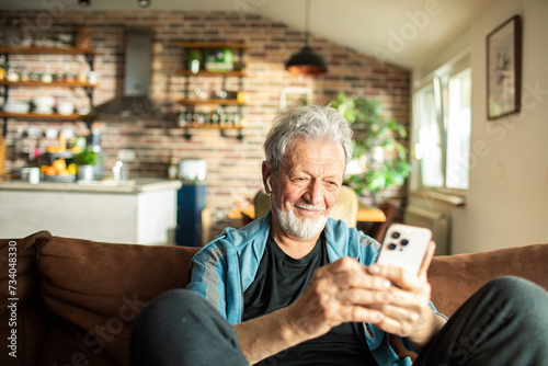 Senior man using a smartphone on the sofa at home photo