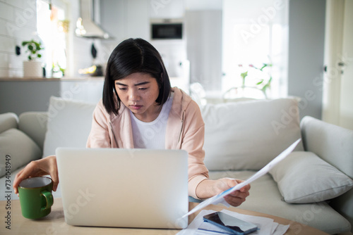 Young woman thinking about bills at home with laptop photo
