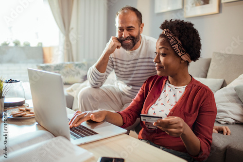 Diverse middle aged couple using laptop for online shopping at home photo