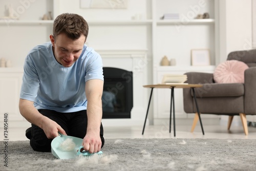 Smiling man with brush and pan removing pet hair from carpet at home. Space for text