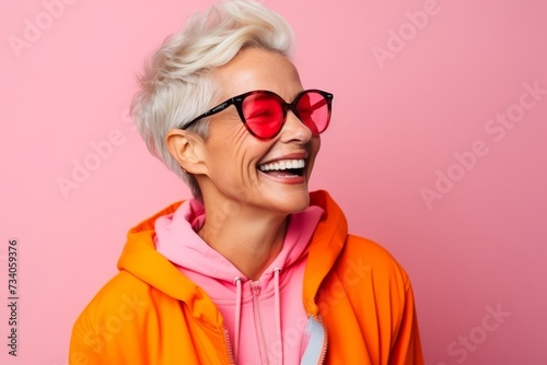 Portrait of a happy senior woman in sunglasses over pink background. © Loli