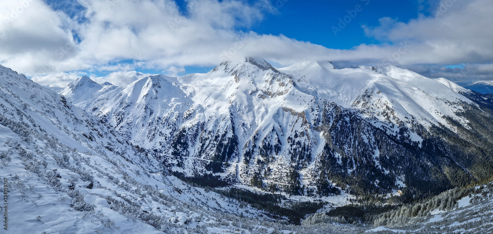 Aerial panoramic view above the Pirin mountains with rocky peaks covered with snow. Winter view at Bansko ski resort in Bulgaria