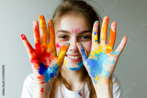 Smiling girl playing with colors  paint on hands and face  showing the two hands full of colorful