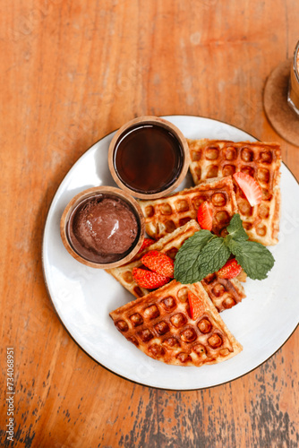 Belgian waffles with strawberry, chocolate and honey on plate top view. Crispy delicious waffles on wooden background