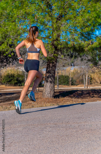 A fit girl runner, on her back, dressed in tight shorts and a tight sports t-shirt, running with style and perfect technical movements with her legs stretched along an asphalt path in a nature park. © sirbouman