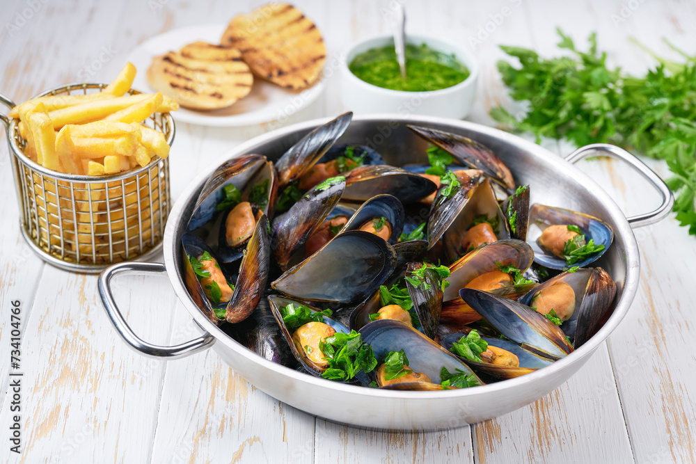 traditional belgian dish steamed mussels with french fries on a white wooden table. traditional belgian dish steamed mussels with french fries on a white wooden table.