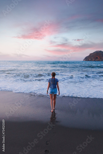 A young girl walks along the beach to the sea during sunset