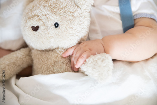 Hand of a little child holding a soft beige teddy bear child walking in white clothes lying in a white bedtime story bedtime dream child
