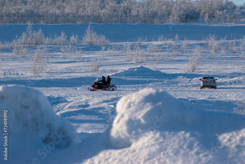 People riding snowmobiles and waving hands on the frozen lake in winter, Scandinavian landscape.