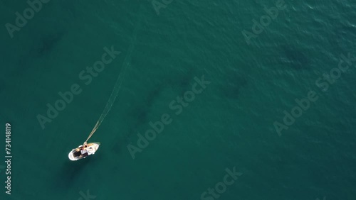 drone, vista dall'alto. Pescatore su piccola barca in mare limpido raccoglie rete da Pesca. Movimento a salire. photo