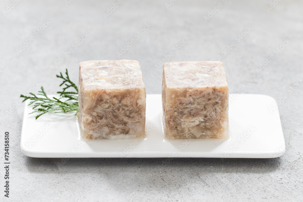 Aspic. Cold appetizer. Chicken jellied meat in the shape of a cube. On a plate. Light grey background. Close up Aspic. Cold appetizer. Chicken jellied meat in the shape of a cube. On a plate. Light grey background. Close up