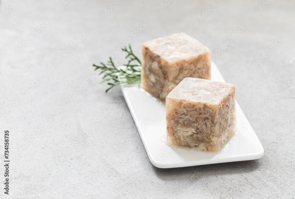 Cold appetizer. Chicken jellied meat in the shape of a cube. On a plate. Light grey background. Copy space