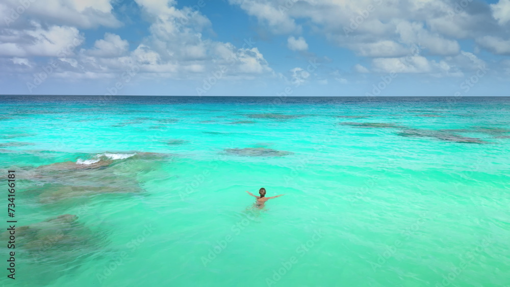 Woman swimming on waves in open sea coral reef. Blue water, tropical exotic island. Outdoor lifestyle travel on summer holiday vacation. Panoramic drone view