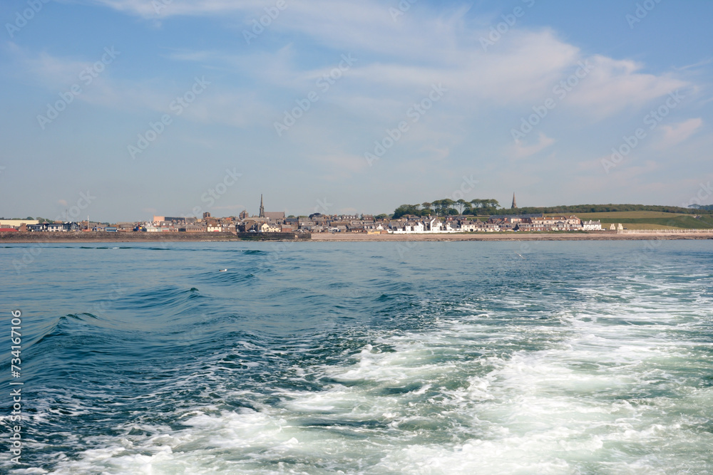 View from a boat in the sea to the old city on the shore on the horizon. Foamy waves spread from the boat