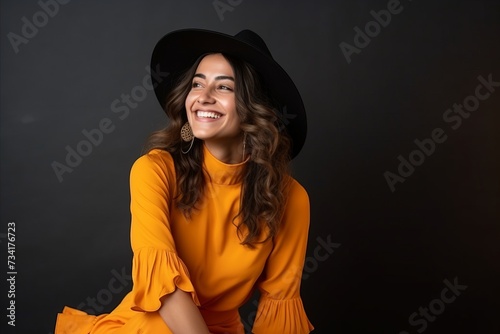 Beautiful young woman in orange dress and black hat on black background