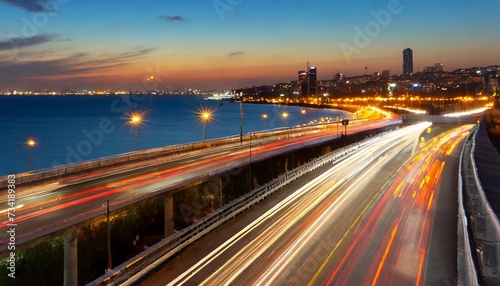 the motion blur of a busy urban highway during the evening rush hour the city skyline serves as the background illuminated by a sea of headlights and taillights © Claudio