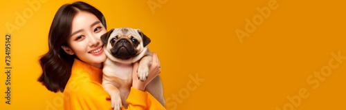 The image features a young woman dressed in a bright orange shirt with a joyful expression as she lovingly embraces a cute pug. Both the woman and the dog are looking directly at the camera against a 