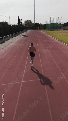 Athlete running on athletics track, tracking from behind, vertical drone video. Motivation and personal work concept. Copy space