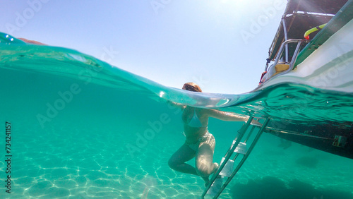 woman in bikini under the sea going down the stairs of the boat in a transparent turquoise blue sea